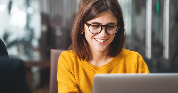 woman in glasses smiling working on laptop