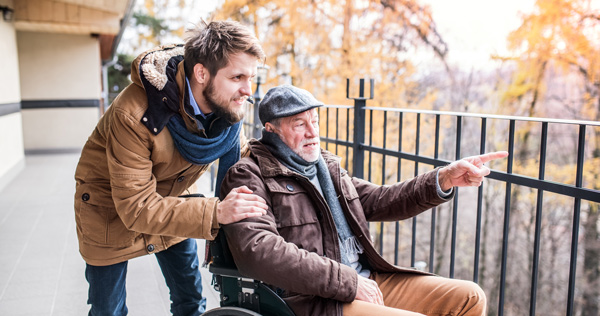 carer and elderly gentleman in wheelchair outside looking at nature